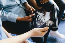 Cropped Hands Of Doctor Showing Ultrasound To Daughter And Mother On Tablet Computer In Hospital