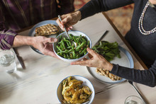 Midsection Of Man Giving Bowl Of Cooked Green Beans To Woman At Dining Table