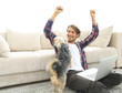 © ASDF - happy guy exults with his dog sitting near the sofa in the living room.