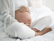 © natsarun - Close up of pregnant woman sitting on bed and touching her belly in bedroom at home