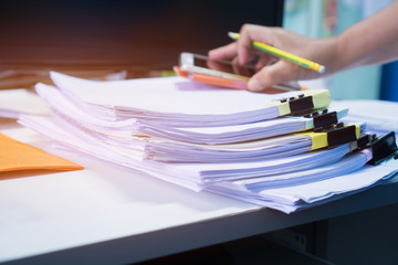 Wall Mural - Business Documents concept : Businessman hands working in Stacks paper files, use smartphone computer for searching or checking unfinished document achieves with clip papers on busy work desk office