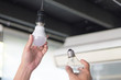 Power saving concept. Asia man changing compact-fluorescent (CFL) bulbs with new LED light bulb.