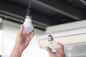 Power saving concept. Asia man changing compact-fluorescent (CFL) bulbs with new LED light bulb.