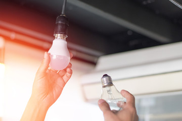 power saving concept. asia man changing compact-fluorescent (cfl) bulbs with new led light bulb.