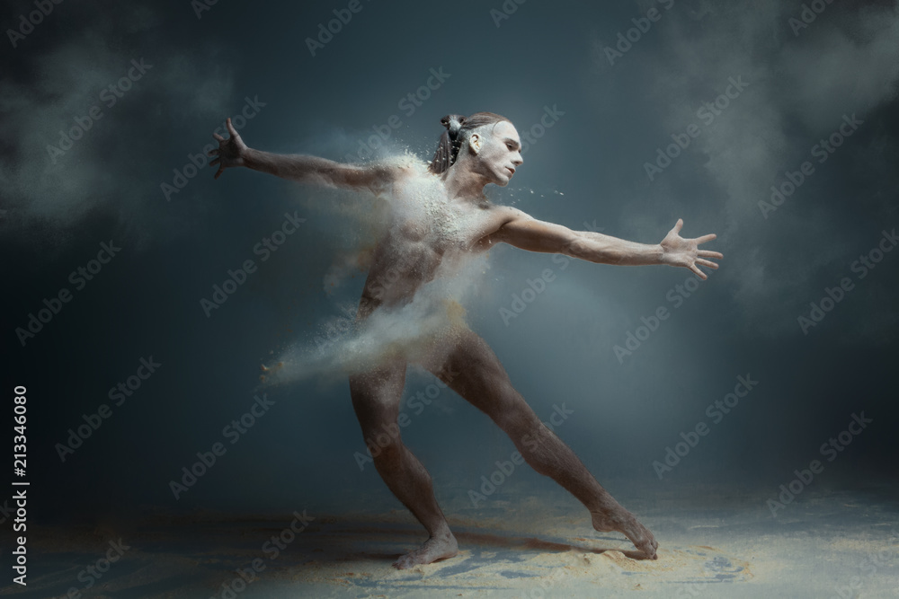 Dancing in flour concept. Long hair muscle fitness guy man male dancer in dust / fog. Guy wearing white shorts making dance element in flour cloud on isolated grey background - obrazy, fototapety, plakaty 