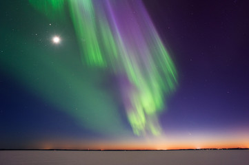 northern lights and moon above frozen lake after sunset in eastern finland