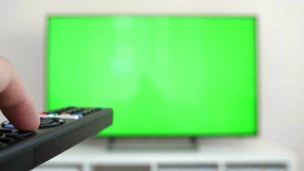 Watching tv with green screen at home interior. Push buttons on remote. Changing channels on television