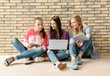 © Africa Studio - Cool teenage girls with modern devices sitting on floor near wall