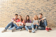 © Africa Studio - Teenagers with modern devices sitting on floor near wall