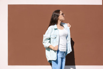 Wall Mural - Young hipster woman in stylish jeans and jacket posing near color wall