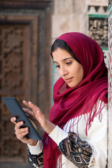 Muslim woman working on tablet in traditional clothing with red headscarf on her head