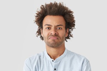 Wall Mural - Negative human facial expressions concept. Curly African American male purses lips, has angry look, being dissatisfied with not delicious supper cooked by wife, suggests go in restaurant instead