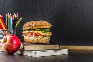 Healthy school food concept, lunch with apple, sandwich, books and alarm clock on chalkboard background copy space