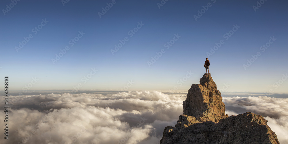 On the top of the world. Man on top of the mountain above the clouds. - obrazy, fototapety, plakaty 