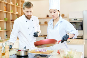 Portrait of Asian female chef  holding frying pan over stove in modern restaurant kitchen, copy space