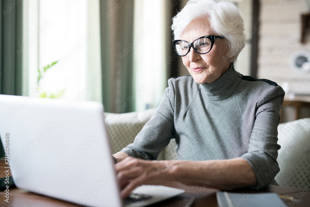 White haired senior woman wearing eyeglasses sitting at cafe and using her laptop - obrazy, fototapety, plakaty 