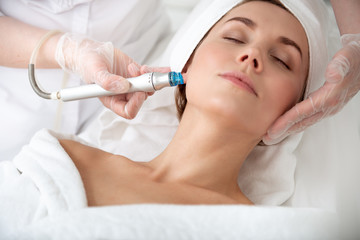 Portrait of calm girl getting massage with special apparatus machine. Therapist holding it in hands