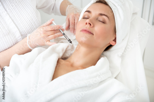 Fotografía Portrait of smiling lady lying on bed while getting beauty injection in neck