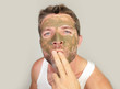 © TheVisualsYouNeed - attractive and happy man with green cream on his face applying facial mask sending kiss to his reflection in mirror feeling conscious in male cosmetics concept