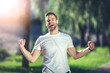 It is my life. Waist up portrait of smiling young man singing with earphones during jogging. He is clenching fists with delight and closing eyes in joy