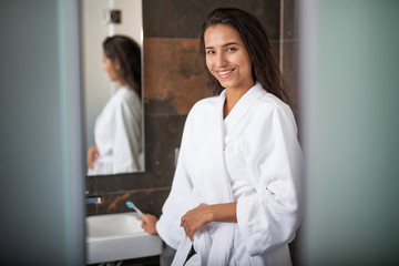 Wall Mural - Portrait of beaming woman with attractive smile keeping toothbrush while looking at camera. She wearing fluffy bathrobe