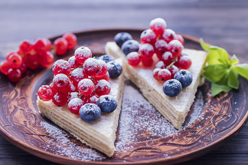 Two pieces of puff cake with fresh berries and sugar powder on brown plate and two brown cups of coffee on dark wooden table.