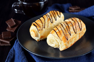 Two golden buns decorated with chocolate on a dark plate