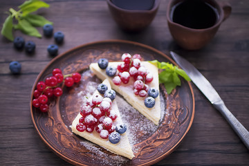 Two pieces of puff cake with fresh berries and sugar powder on brown plate and two brown cups of coffee on dark wooden table.