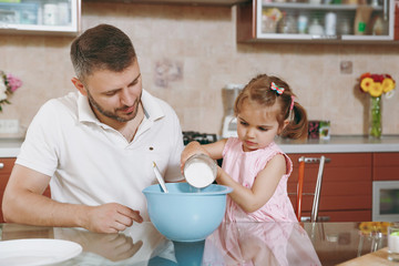 Little kid girl helps man to cook Christmas ginger cookies, pour flour into bowl at table. Happy family dad, child daughter cooking food in weekend morning. Father's day holiday. Parenthood childhood.