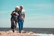 Affectionate senior couple moving along coastline by seaside at summer resort