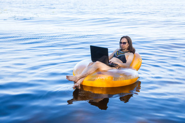 Wall Mural - Business woman working on a laptop in an inflatable ring on the sea, the concept of working on vacation.