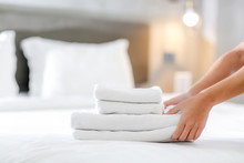 Close-up Of Hands Putting Stack Of Fresh White Bath Towels On The Bed Sheet. Room Service Maid Cleaning Hotel Room.