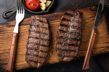 Closeup ready to eat steak Top Blade beef breeds of black Angus with grill tomato, garlic and on a wooden Board. The finished dish for dinner on a dark stone background. Top view