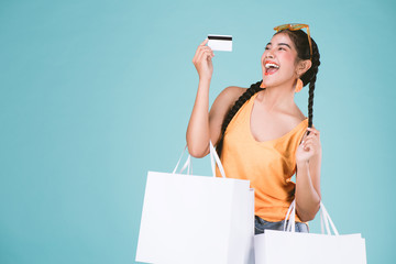 portrait of cheerful young brunette woman holding credit card and shopping bags over Blue background.