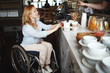 Woman in a wheelchair buys coffee and buns in a cafe.