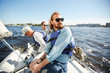 Content carefree young bearded man in sunglasses enjoying yachting with friends: he sitting on deck and contemplating seascape