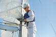 © pressmaster - Serious skilled mature sailor in sunglasses and cap wearing stylish outfit fixing mainsail on mast with rope