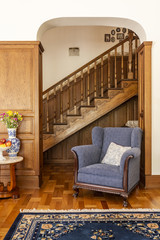 Wall Mural - Blue armchair against wooden stairs in classic living room interior with flowers and carpet. Real photo