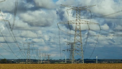 Wall Mural - Time lapse of high voltage power lines, transmission towers and wind turbines in agricultural fields on a bright summer day with clouds in the sky. Electric power industry and nature concept