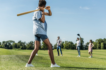 Wall Mural - african american teenager holding baseball bat and playing with friends in park