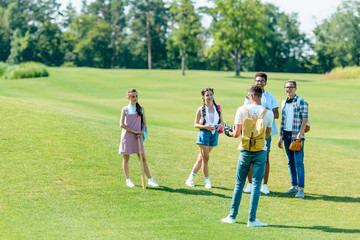 Wall Mural - happy multiethnic teenage classmates with backpacks playing baseball in park