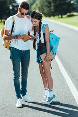 Wall Mural - smiling teenage boy and girl with backpacks looking at notebook in park