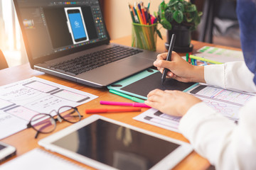 Artist creative designer hands sketching of screens for mobile responsive website development with UI/UX. Developing wireframe sketch layout design mockup on smartphone screen.