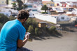 © simona - man from backside using cellular phone with internet connection and app. old town and beach in the background. summer time and leisure activity relaxing