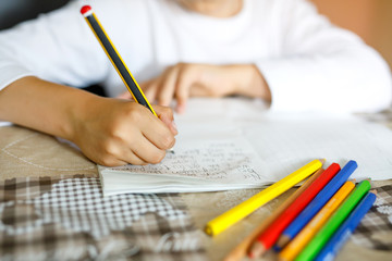 Child doing homework and writing story essay. Elementary or primary school class. Closeup of hands and colorful pencils