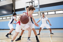 Male High School Basketball Team Dribbling Ball On Court