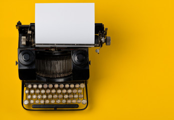 Vintage typewriter top down flatlay shot from above with empty, blank sheet of paper on yellow