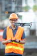 © zephyr_p - Young Asian engineer man flying drone over construction site. Using unmanned aerial vehicle (UAV) for land and building site survey in civil engineering project.