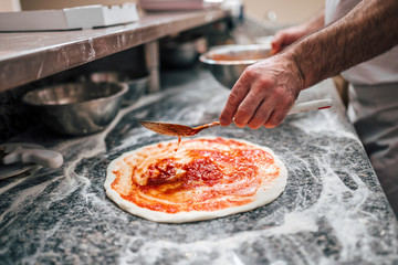 Preparing pizza. Chef's hand adding tomato sauce on pizza dough.