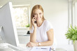 © gzorgz - Young professional woman making a call on her mobile phone while working on computer. Home office